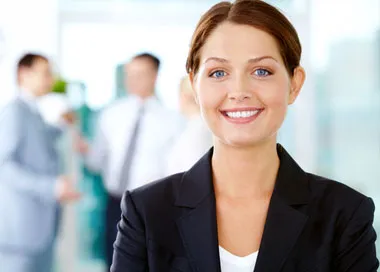 A smiling businesswoman in a dark suit with colleagues talking behind her