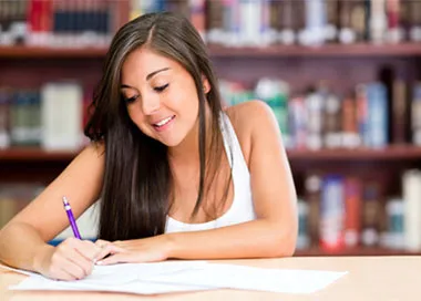 A young woman signing papers at a desk in front of library shelves