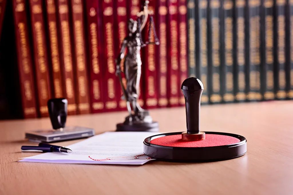 Lady Justice statue, law books and an ink stamp on a notary's desk